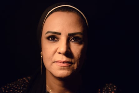 A middle-aged woman in a headscarf against a black background