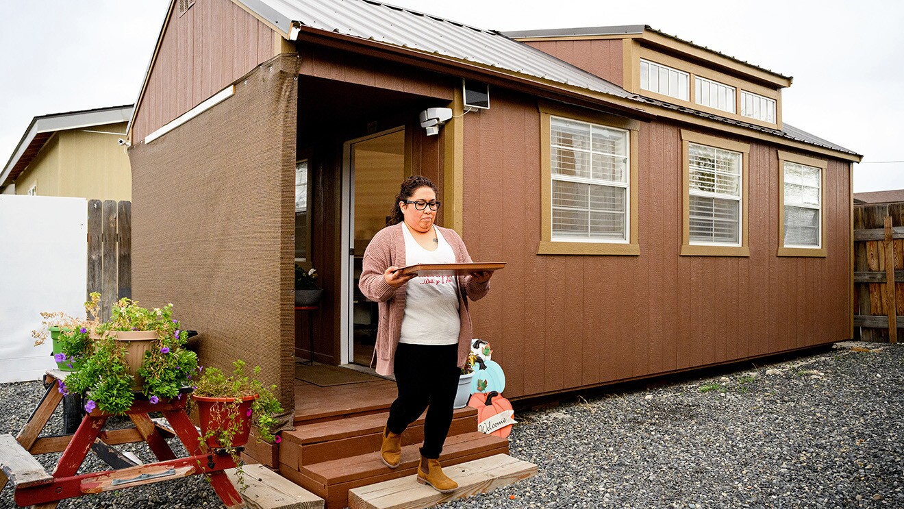 A photo of a baker carrying a sheet of cookies outside of her home.