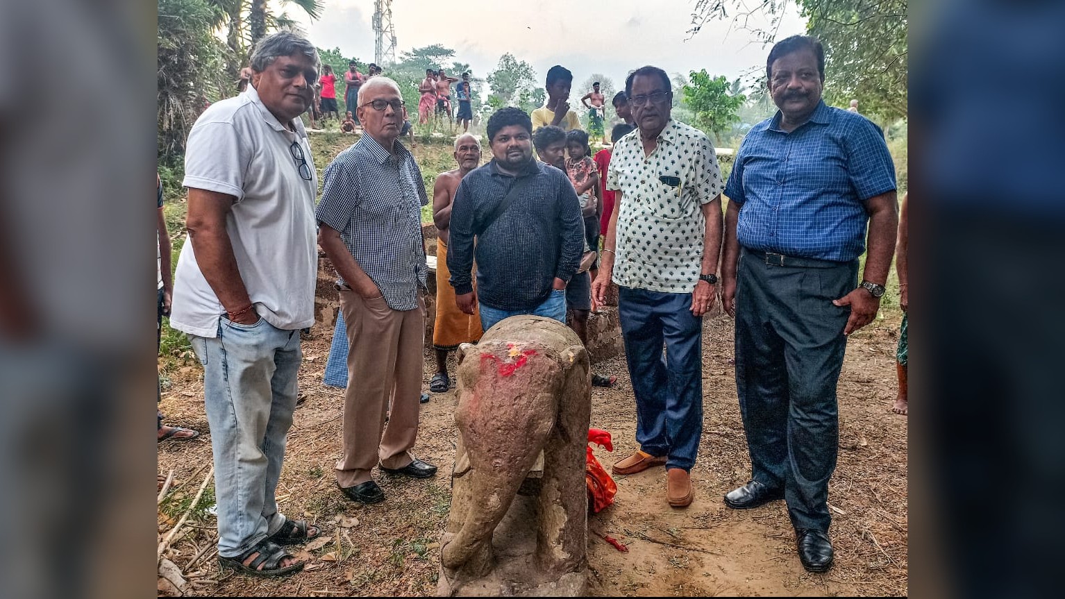 A team of 5 men stand around the elephant statue in the field.