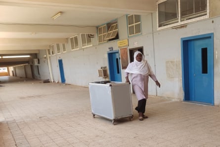 A woman in a headscarf wheels a cart along a deserted walkway 