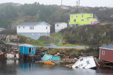 The wreckage of wooden buildings sit in the water along the shoreline