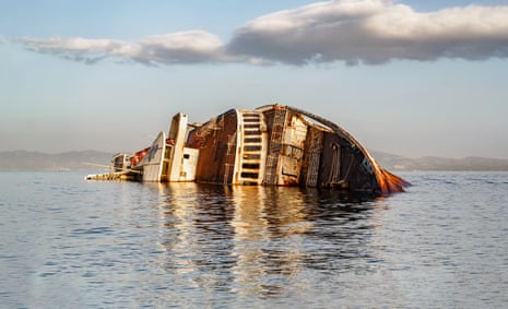A ship lies on its side with only half visible above the water
