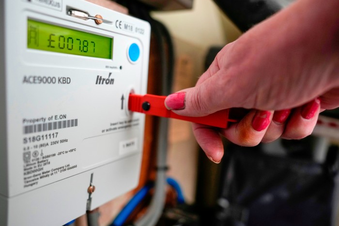 A close-up of a woman’s hand inserting a red key into a prepayment meter at a rented house in Birmingham