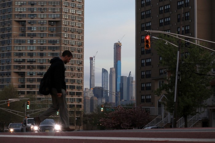 A man walks along a road with the New York high-rise buildings behind him