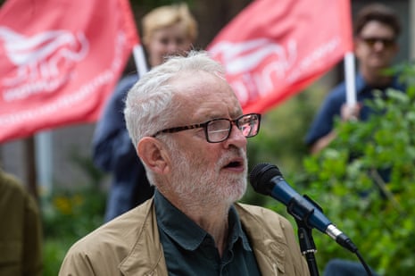 Jeremy Corbyn speaking into a microphone with people waving red flags behind him