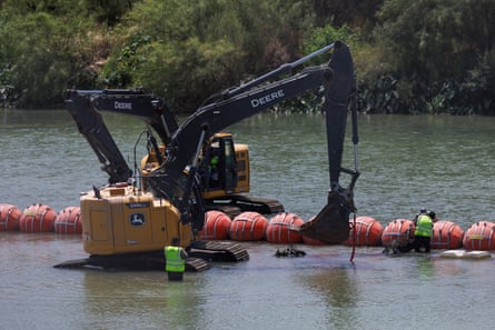 Heavy cranes adjust the red buoy barrier in the river.