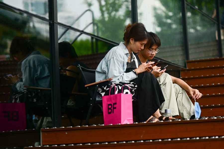 People use their phones outside a shopping centre in Beijing, China on 17 August 2023. (Pedro Pardo/AFP)