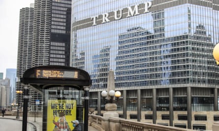 A windowed high-rise building with the word in white ‘Trump’ halfway up, looming over a bend in a river we assume is below a concrete walkway.