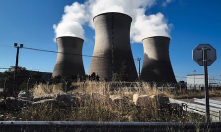 Steam rises from three cooling towers on a raised area of ground
