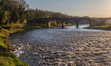 Stone bridge with arches spans the river with green banks and trees to the side