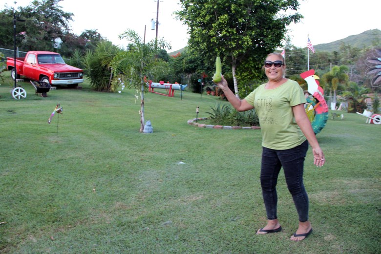 Sol Piñeiro pictured in her yard holding a piece of produce she grew. The sprawling yard is filled with orchids, cacti and colorful artifacts, including a bright red vintage pickup truck.