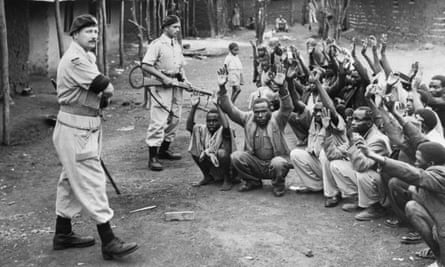 British police hold men from the village of Kariobangi at gunpoint while their huts are searched for evidence that they participated in the Mau Mau rebellion of 1952.