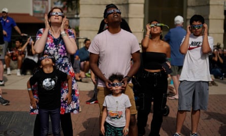 White and brown people, adults and children and teens, standing with necks craned back and glasses on faces