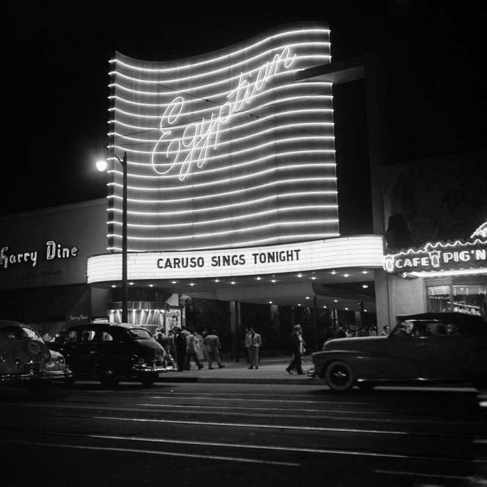 A theatre is lit up at night, advertising ‘Caruso sings tonight’