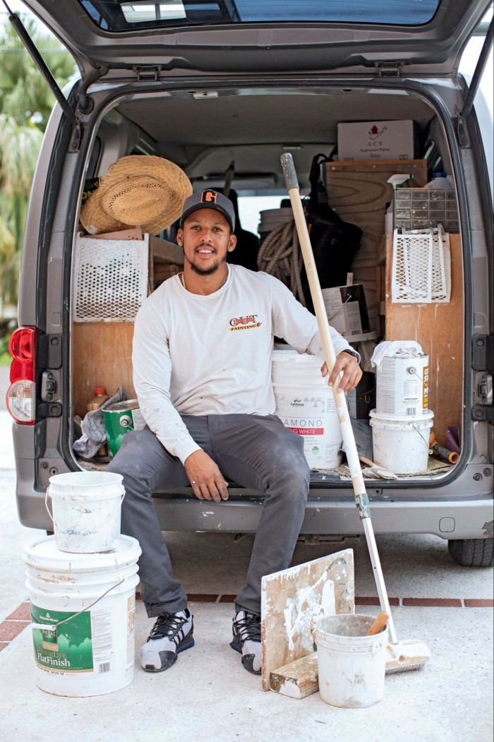 A man in working clothes sitting behind the storage area of a van filled with his tools