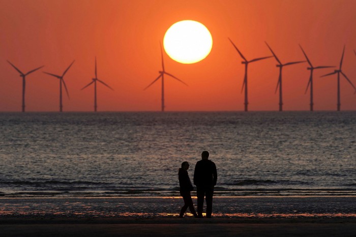 Silhouettes of two people on a beach watching a sunset. Distant wind turbines are also visible