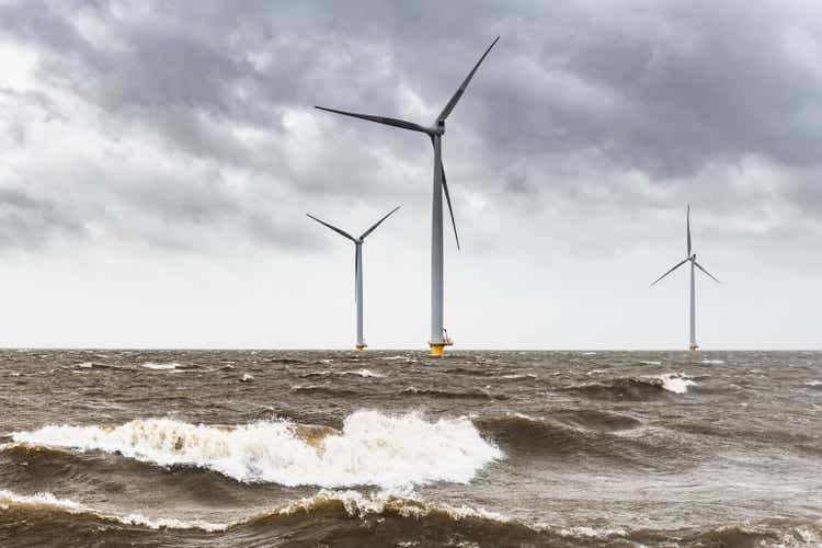 Wind turbines in an offshore wind park during a storm with big waves hitting the shore