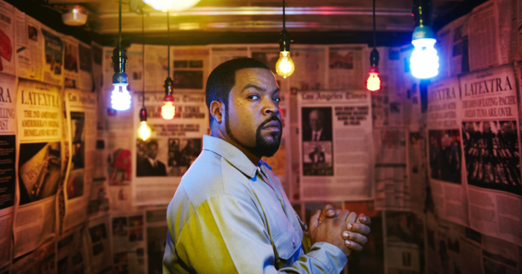 Ice Cube in a room full of light bulbs and newspapers