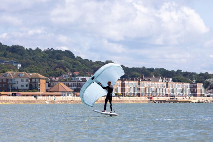 A man kitesurfs with rows of houses on the seafront behind