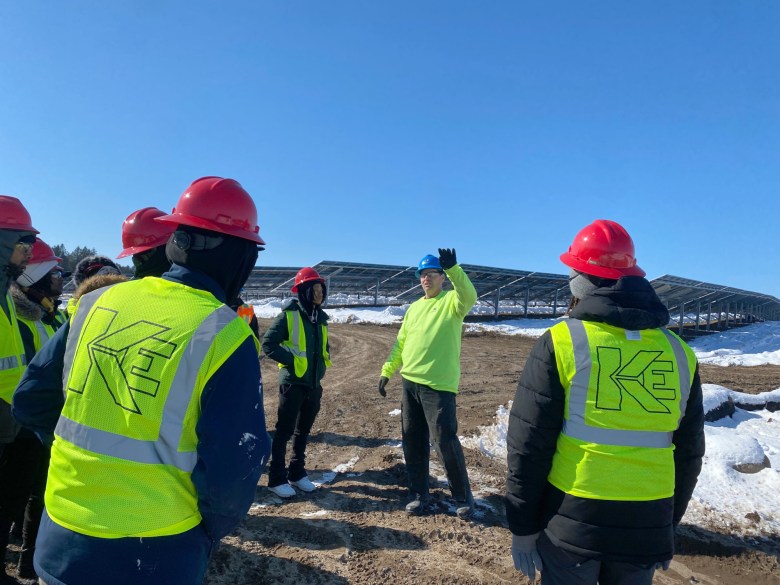 Solar training program participants in day-glo vests and red hard hats at a rural solar array.