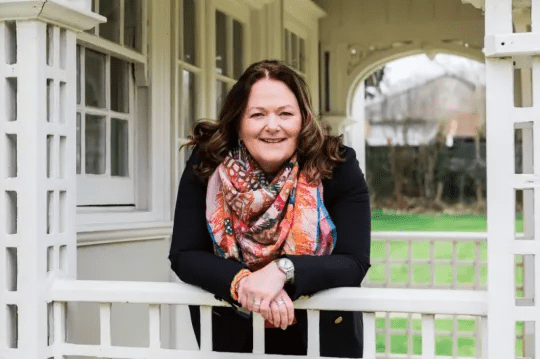 Alison pictured in a colourful scarf, leaning over her patio fence and smiling