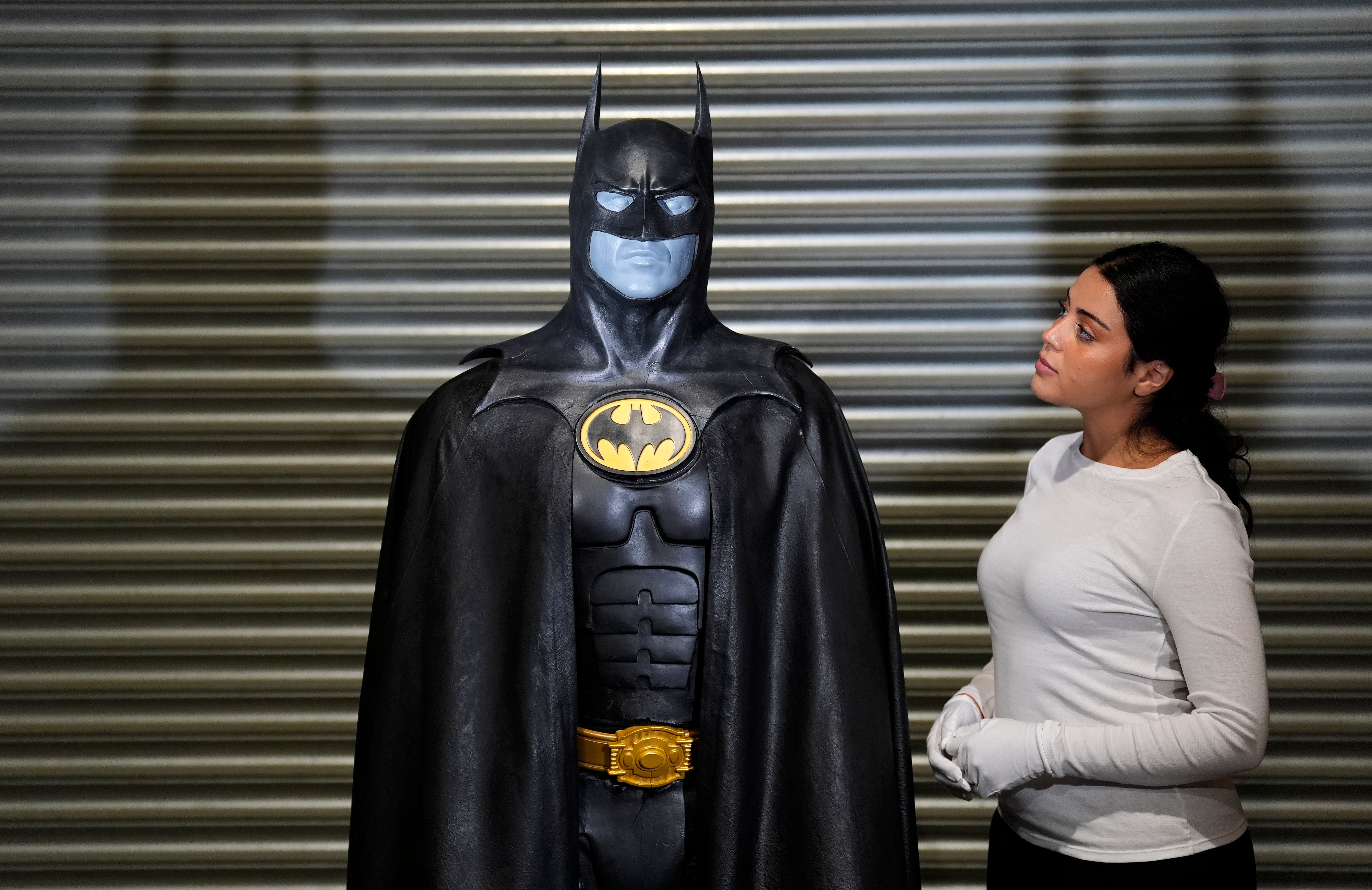 A Propstore employee looks up at Michael Keaton's Batsuit on display from the 1992 film 'Batman Returns'