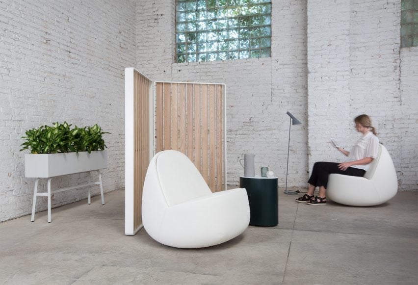 Photo of two rounded, white upholstered Rock lounge chairs in a minimalist lounge area, the one at the back being used by a woman looking at a tablet