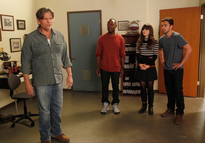 Four people stand in a small office. The room has a desk and shelves