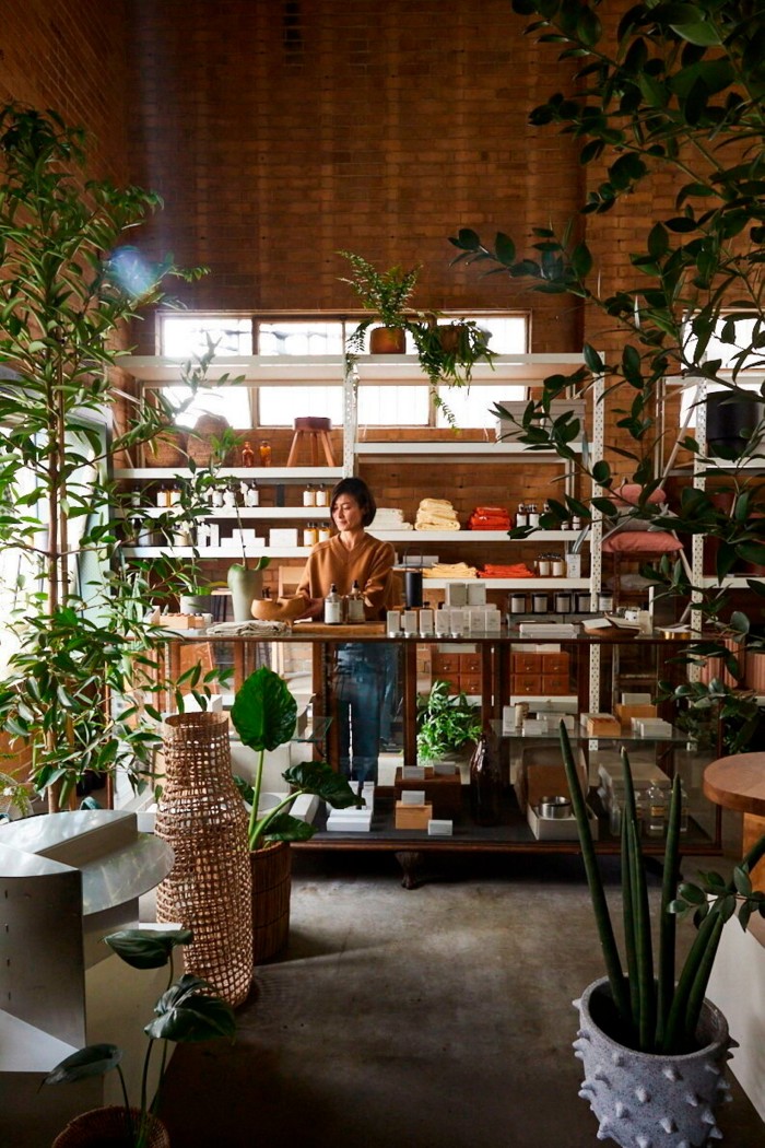 A woman arranges products on a wooden counter, surrounded by natural textiles, ceramics, and minimalist decor