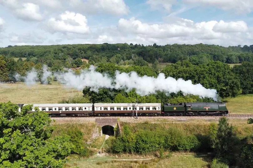 Steam train traveling through a green countryside.