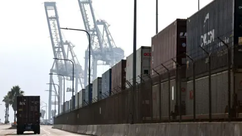 Getty Images A truck drives past shipping containers stacked on rail cars at the Port of Long Beach on December 4, 2024 in Long Beach, California.