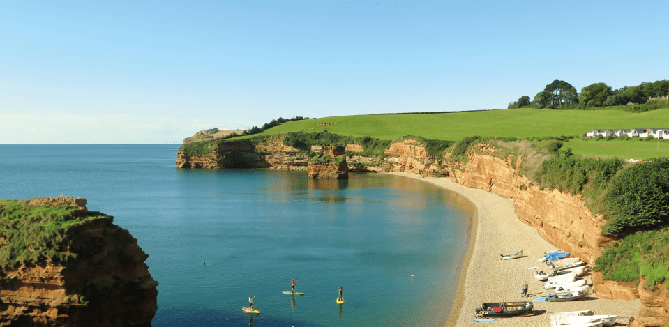 Ladram Bay beach with paddleboarders and boats.