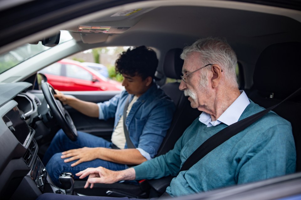 Older man teaching a young man how to drive.