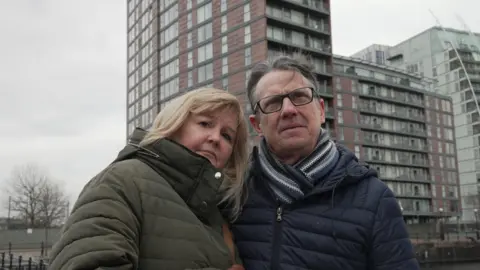 Suzy and Colin standing outside their block of flats in Salford 