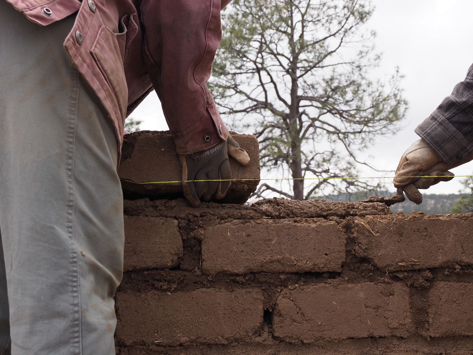 Students work together to trowel mud across a brick before placing another one, which will be leveled to the height of the yellow string.