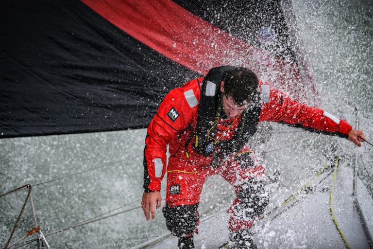 James sailing, standing outside on the boat navigating through a difficult wave