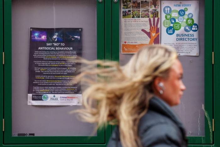 A woman passes a community noticeboard in New Ferry with information on antisocial behaviour