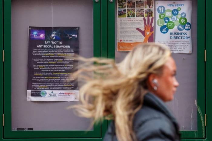 A woman passes a community noticeboard in New Ferry  with information on antisocial behaviour