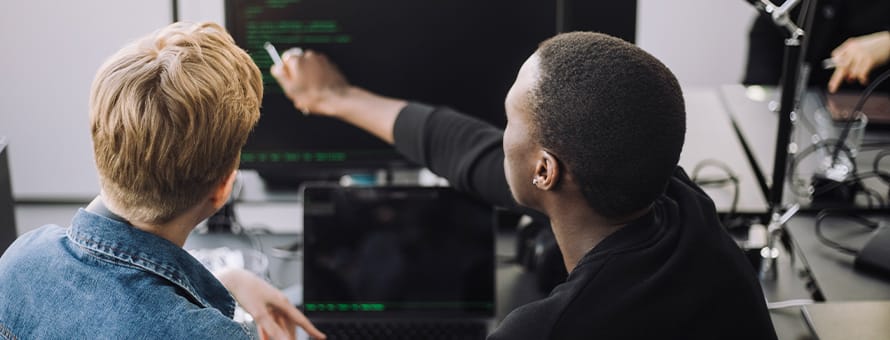 An instructor looking at code on a computer with a student who wants to get into tech.