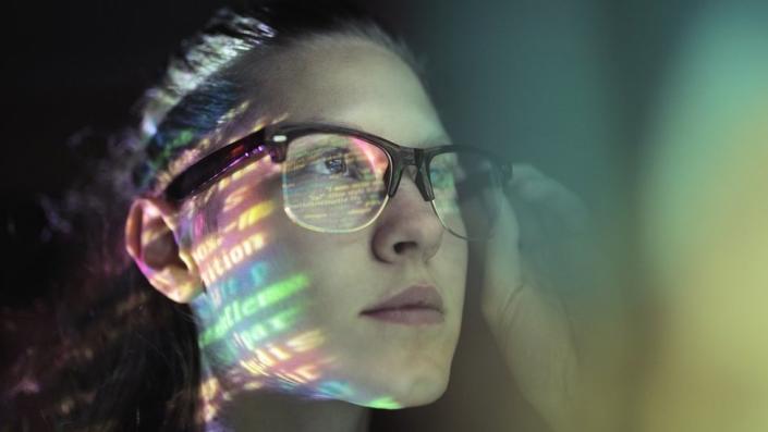 A woman's face is lit up with strings of code