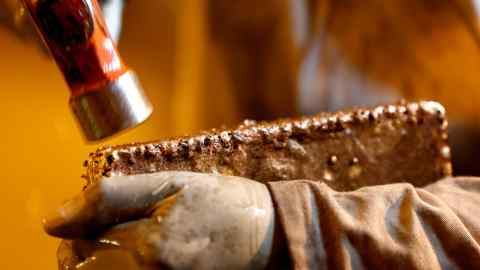 A mine worker hammers the rough surface of a newly molded gold bar