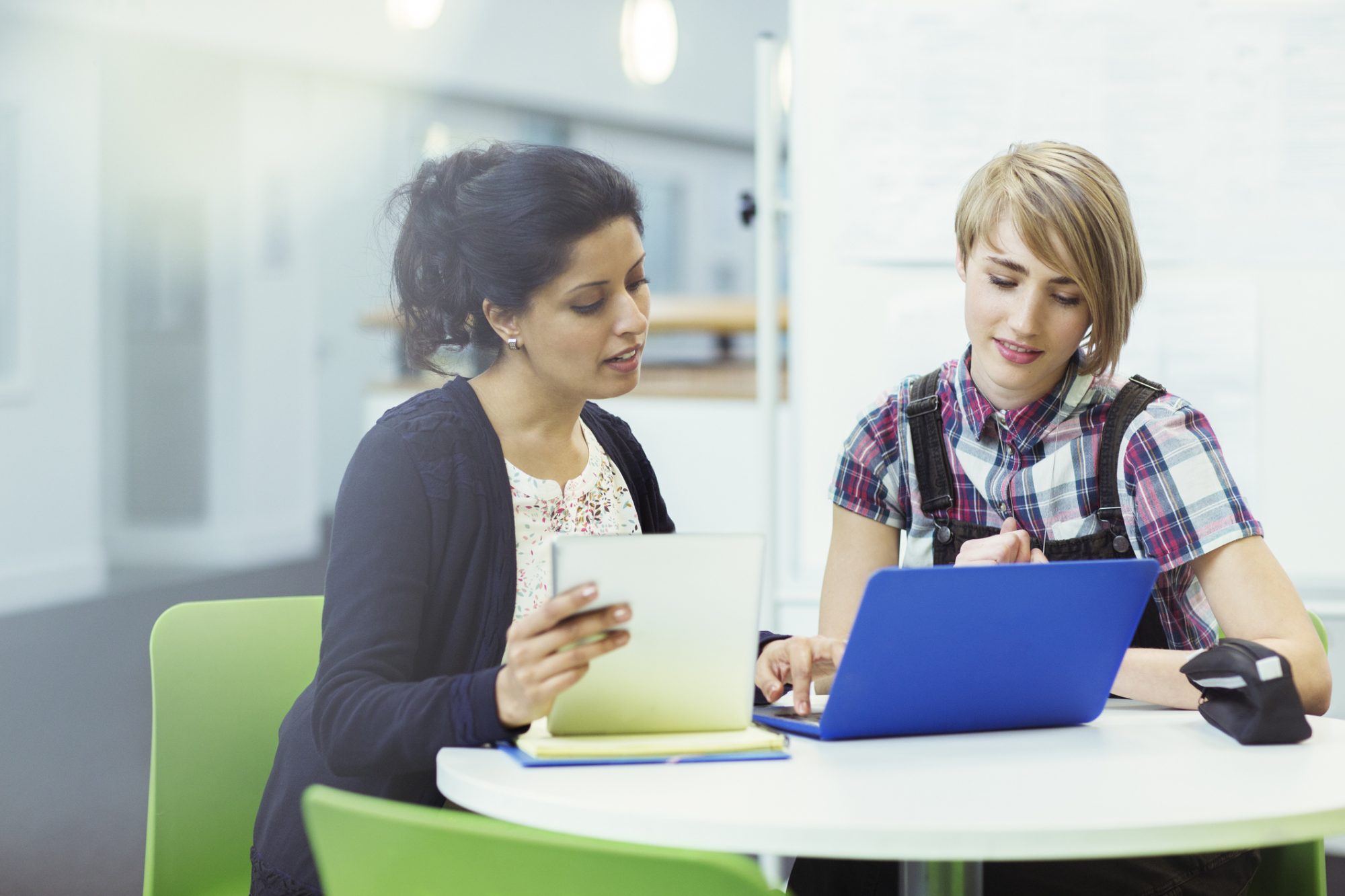 Teacher and student sitting together with digital tablet and laptop