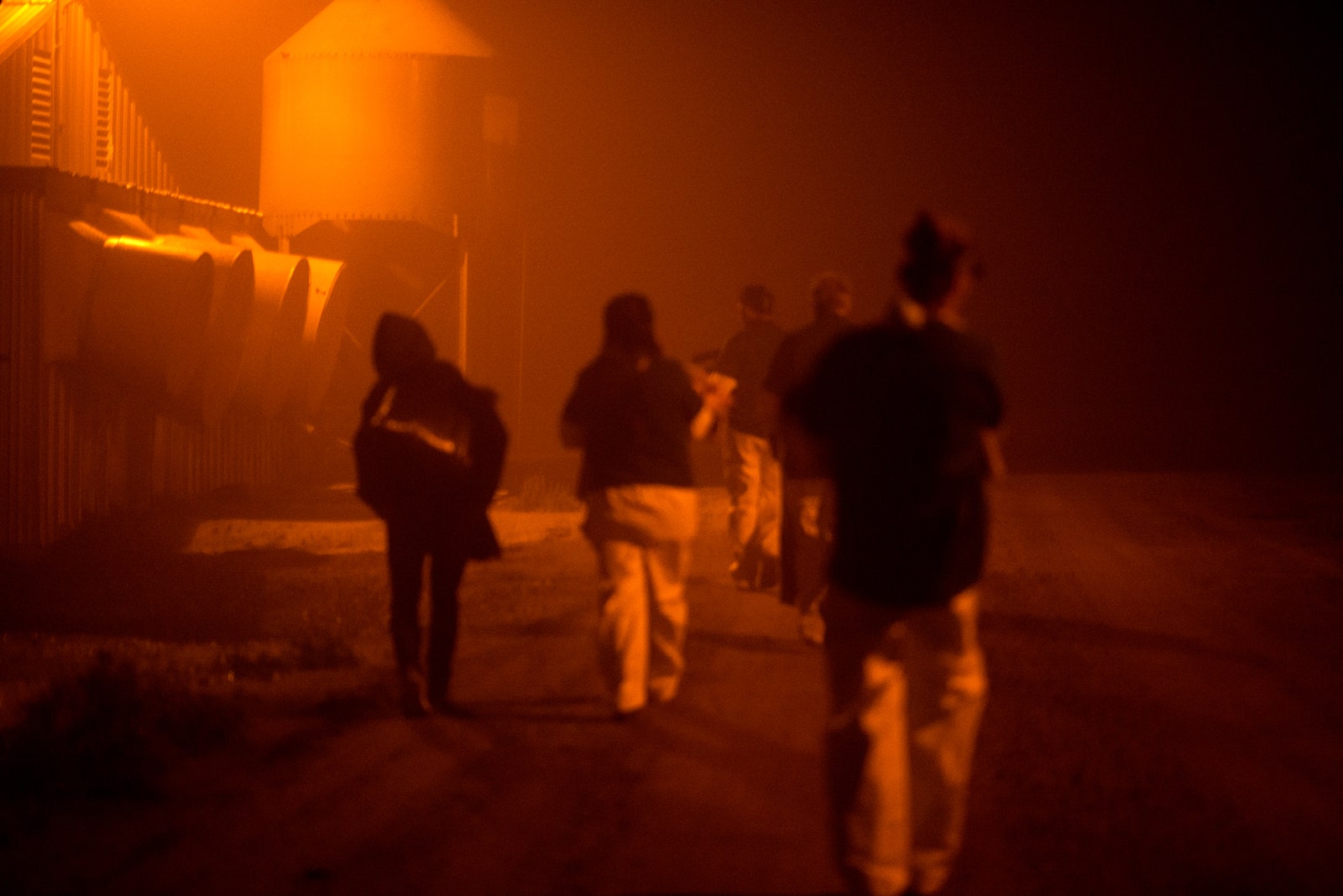 Group of people walking near farm silos at night