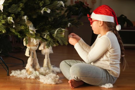 A girl wearing a Santa hat and Christmas glasses decorates a tree with artificial snow and baubles