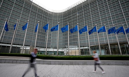 European Union flags wave in the wind as pedestrians walk by the large grey building of the Berlaymont building of the European Commission in Brussels.