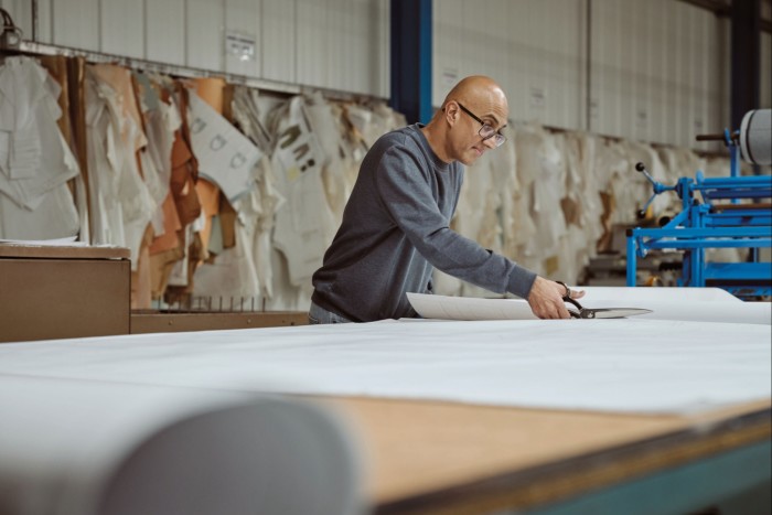 A man cutting a large piece of fabric on a large table
