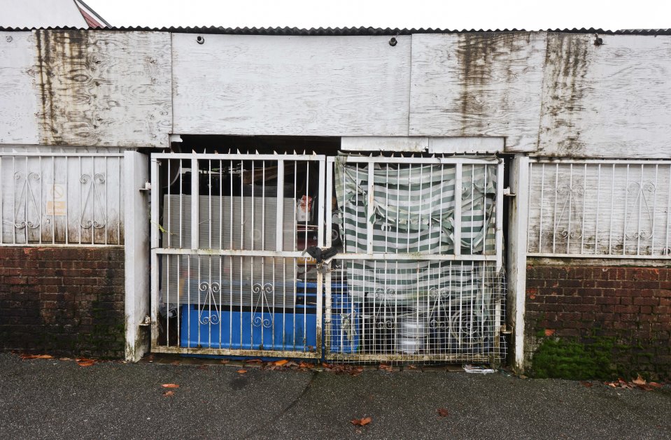 A garage that is filled with cars, rubbish, a kid go kart and speedboat