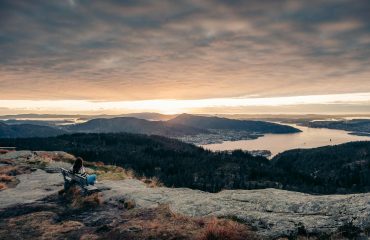 hiker sitting on a bench watching the sunset over the city of bergen from the top of rundemanen mountain
