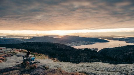 hiker sitting on a bench watching the sunset over the city of bergen from the top of rundemanen mountain