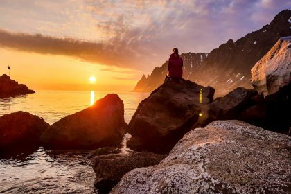 person sitting on rock formation beside body of water